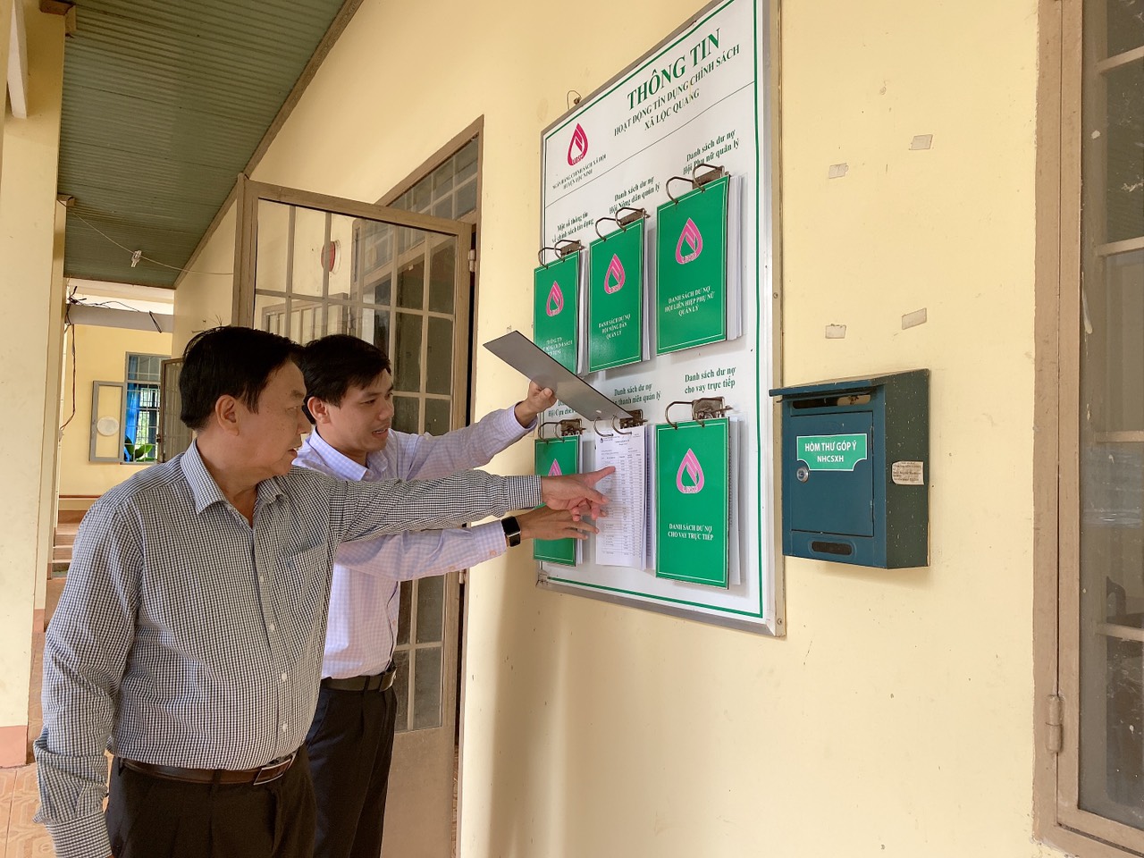 Ông Lê Khắc Phú – Chủ tịch HND huyện (bên trái) kiểm tra thông tin tín dụng chính sách được NHCSXH huyện Lộc Ninh công khai tại điểm giao dịch xã Lộc Quang