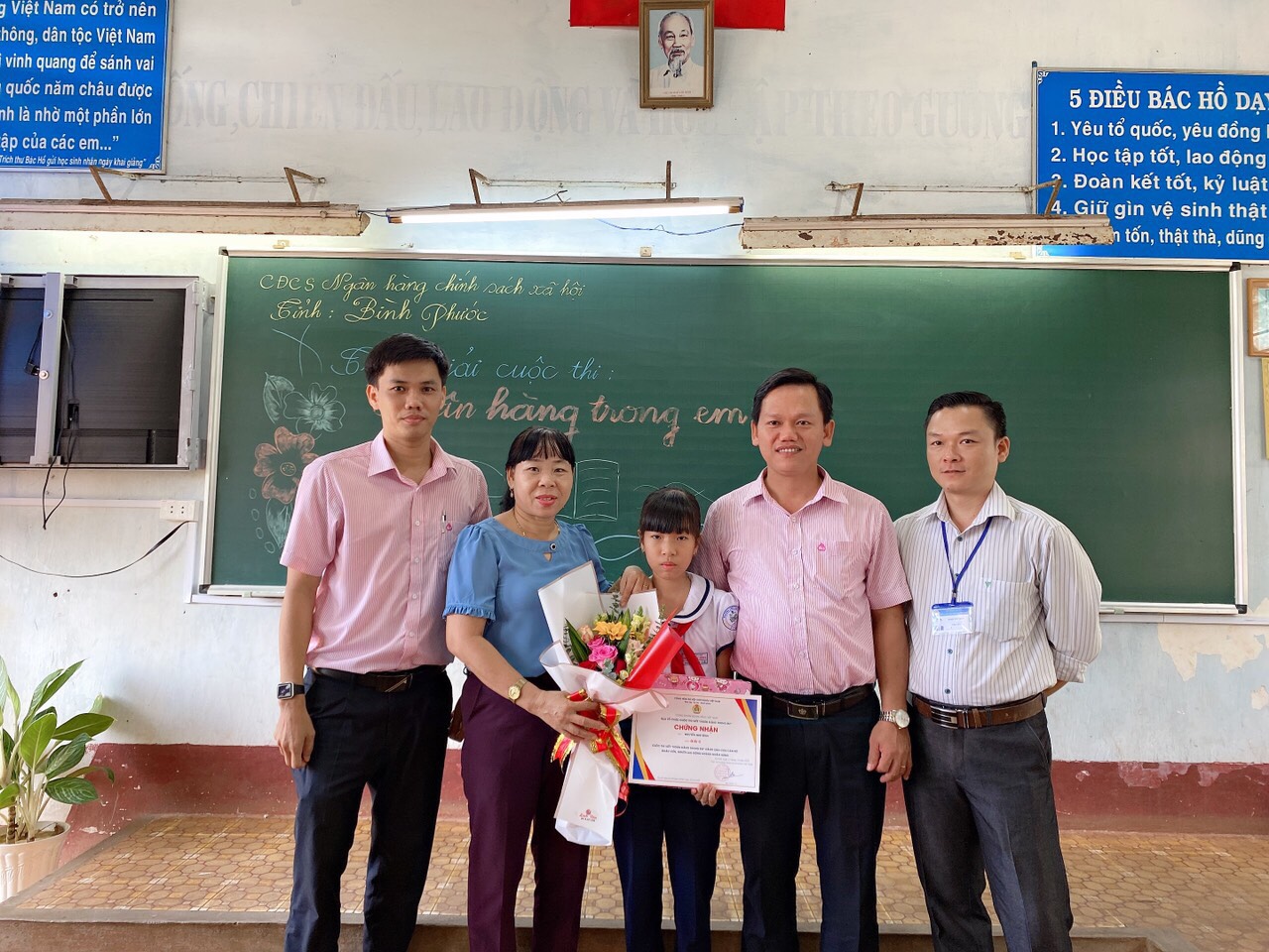 Đại diện lãnh đạo CĐCS NHCSXH tỉnh Bình Phước, Đại diện lãnh đạo trường TH TT Lộc Ninh A trao giấy chứng nhận và phần thưởng cho bé Nguyễn Như Bình